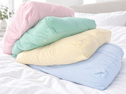 Pastel pink mint yellow and blue Breakup Pillows stacked on a white bed for breakup care package ideas