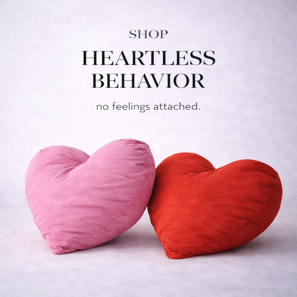 Two heart-shaped pillows, one pink and one red, on a light gray background with text 'SHOP HEARTLESS BEHAVIOR no feelings attached.'.